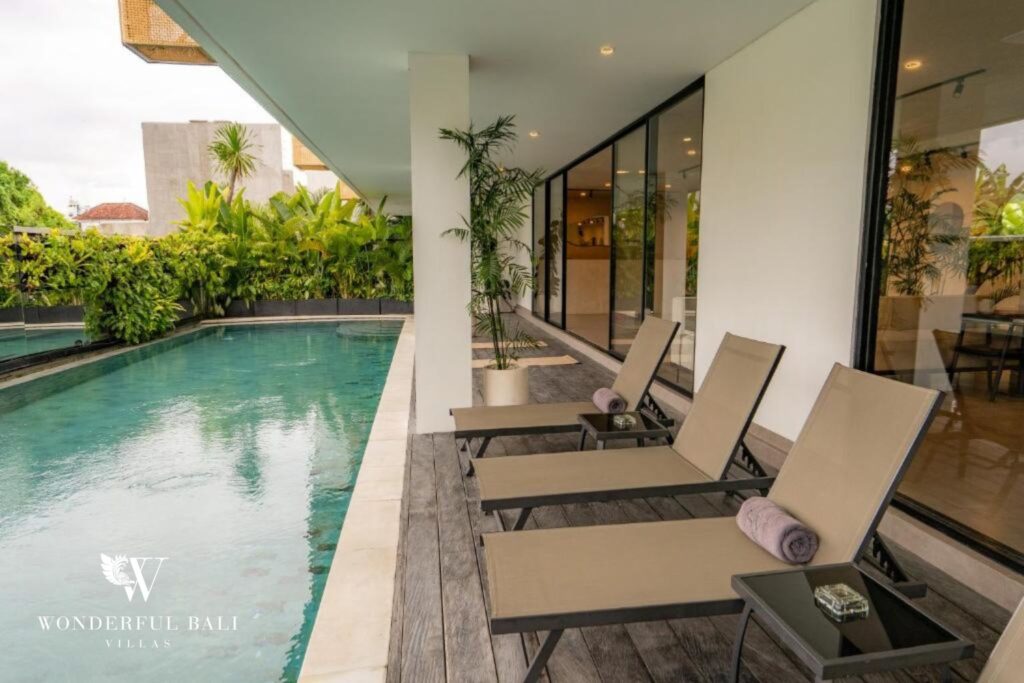 Shared swimming pool with sun loungers on timber deck, modern apartment building in Canggu