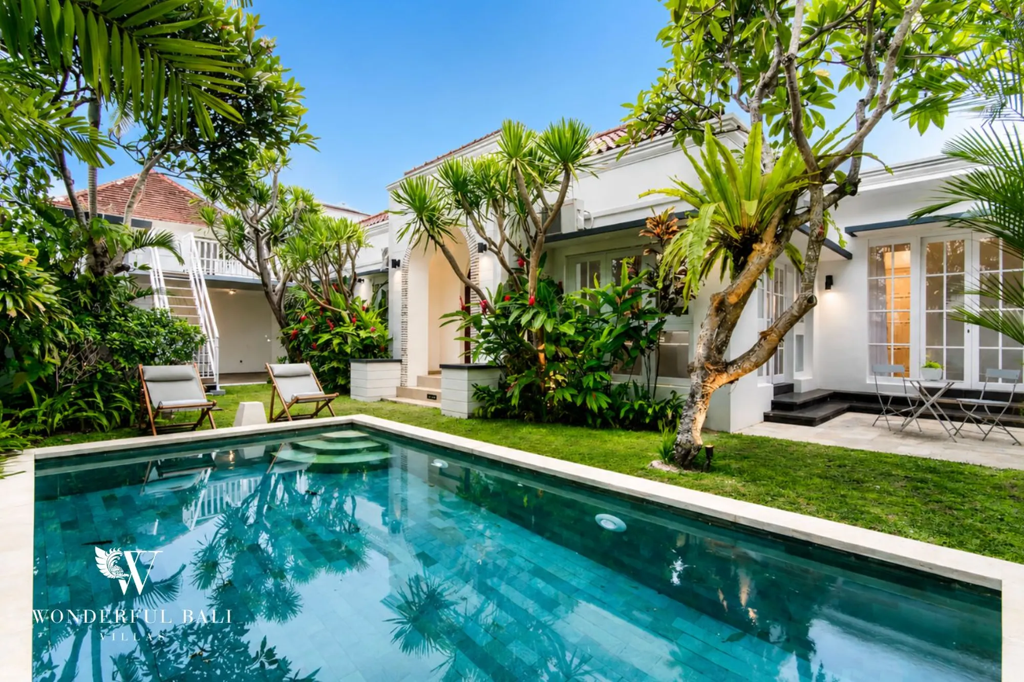 Private pool fronting a white colonial-style villa with manicured garden