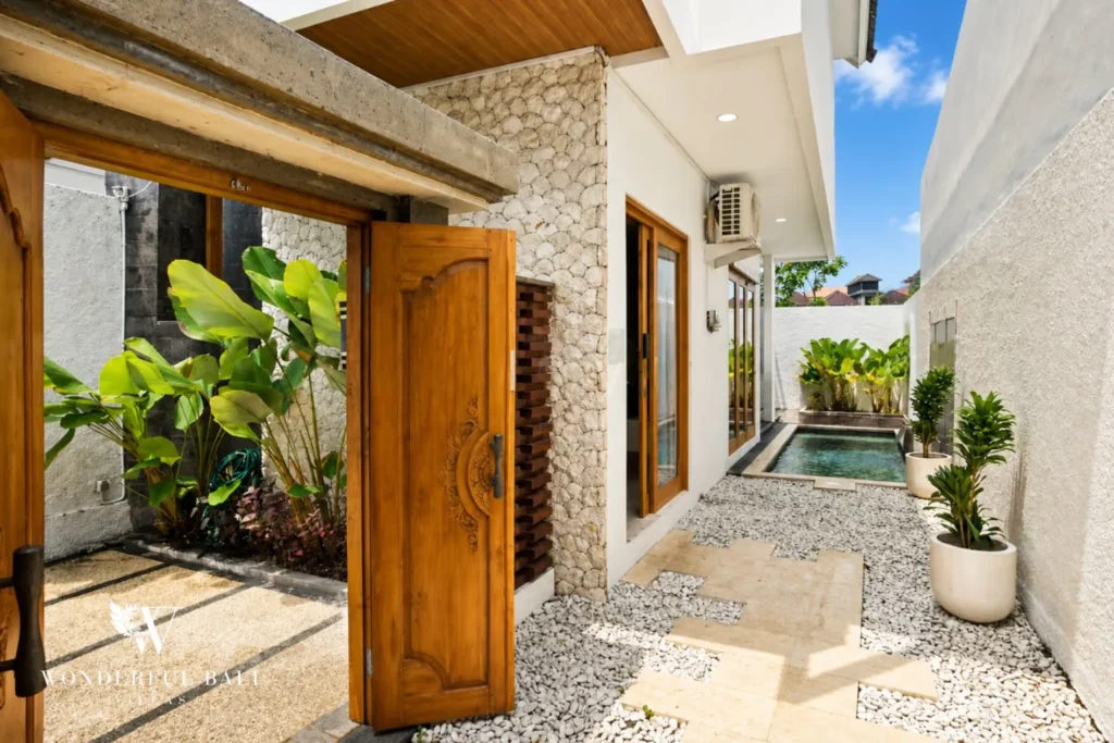 Entrance courtyard with timber door, plants and stone wall at villa in Denpasar, Bali