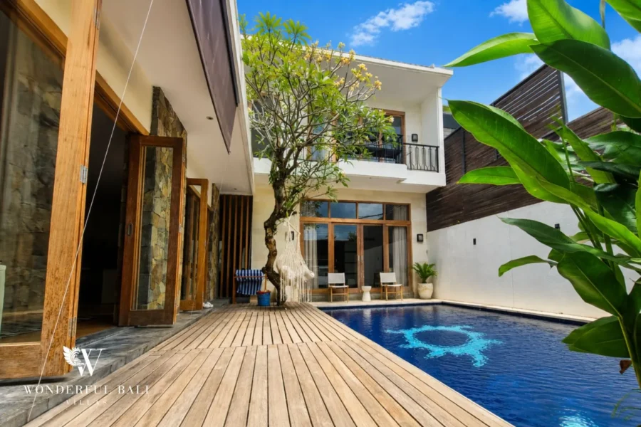 Pool courtyard with stone wall, timber deck and lush plants at dusk at villa in Berawa, Bali
