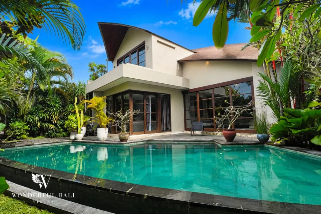 Pool with two-storey villa exterior framed by palms at villa in Umalas, Bali