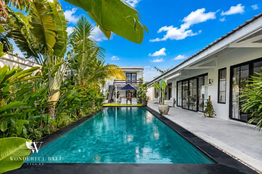 Pool with single-storey villa exterior framed by palms at villa in Canggu, Bali
