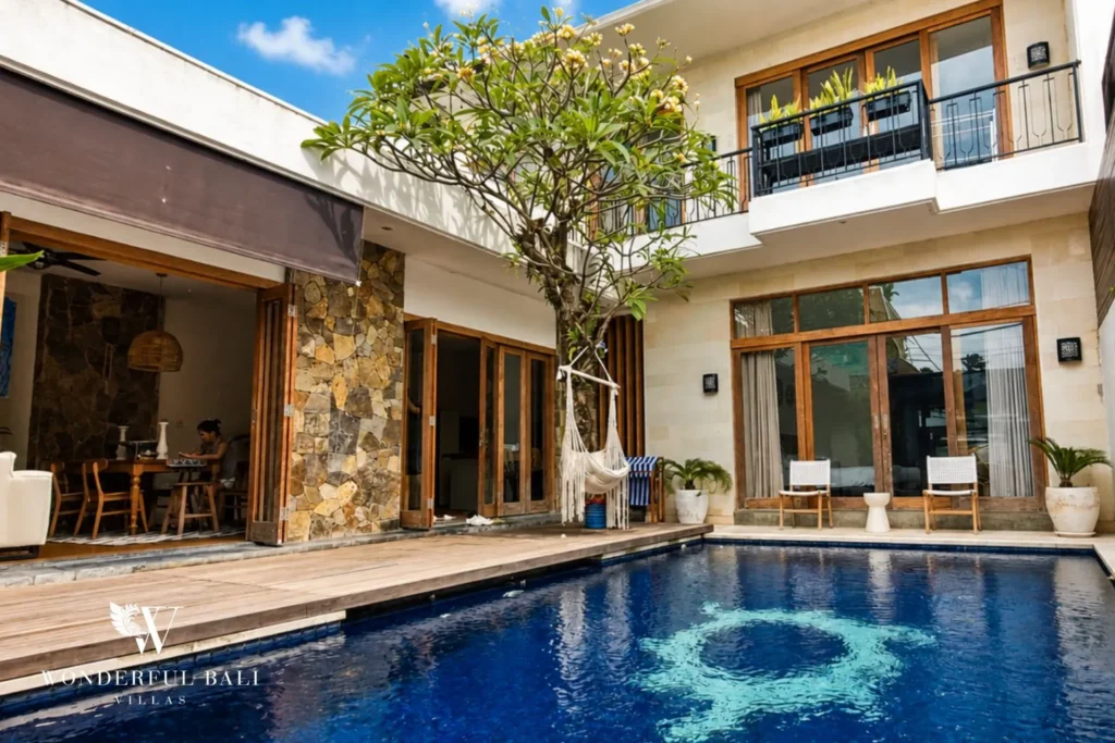 Pool with natural stone feature wall and two-storey villa facade at villa in Berawa, Bali