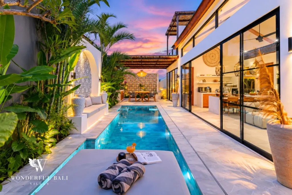 Pool and villa exterior at dusk with glass walls at villa in Seseh, Bali