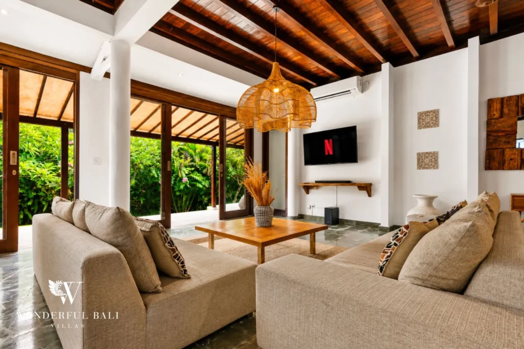 Living area with sofa, TV and exposed timber ceiling open to garden at villa in Umalas, Bali
