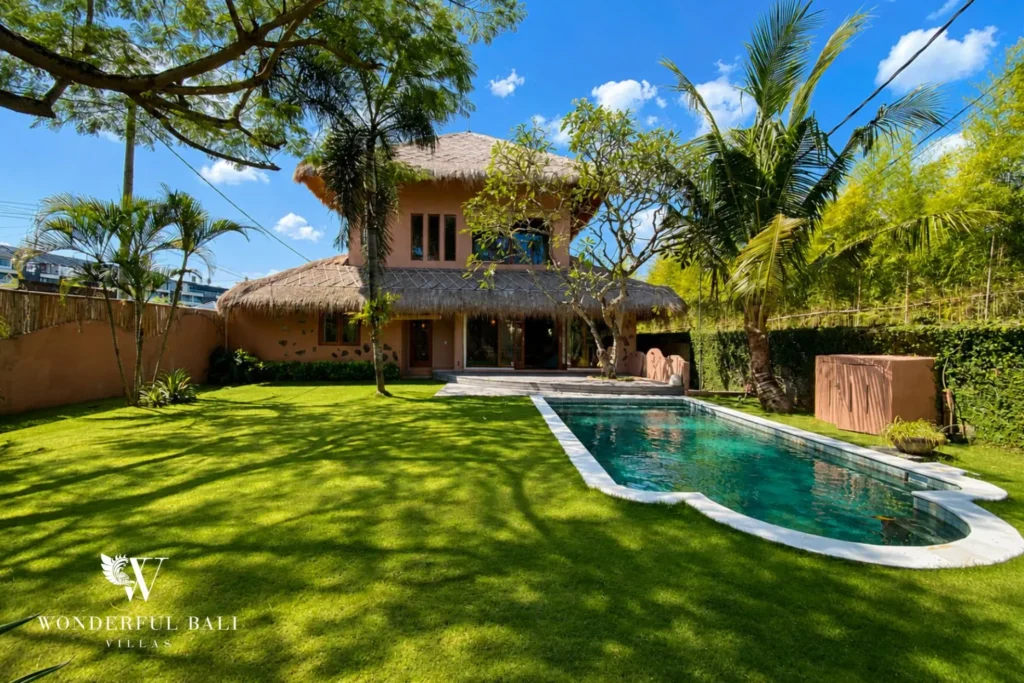 Two-storey villa exterior with lawn and pool in daylight at villa in Bumbak, Bali