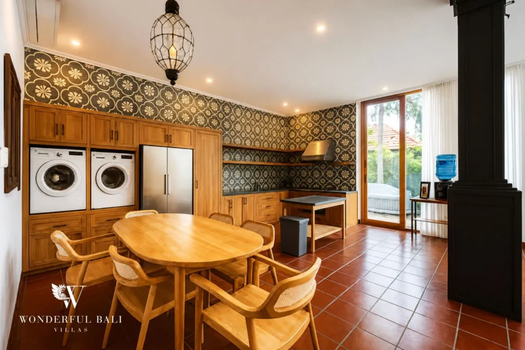 Dining table with rattan pendant light and open kitchen behind at villa in Canggu, Bali