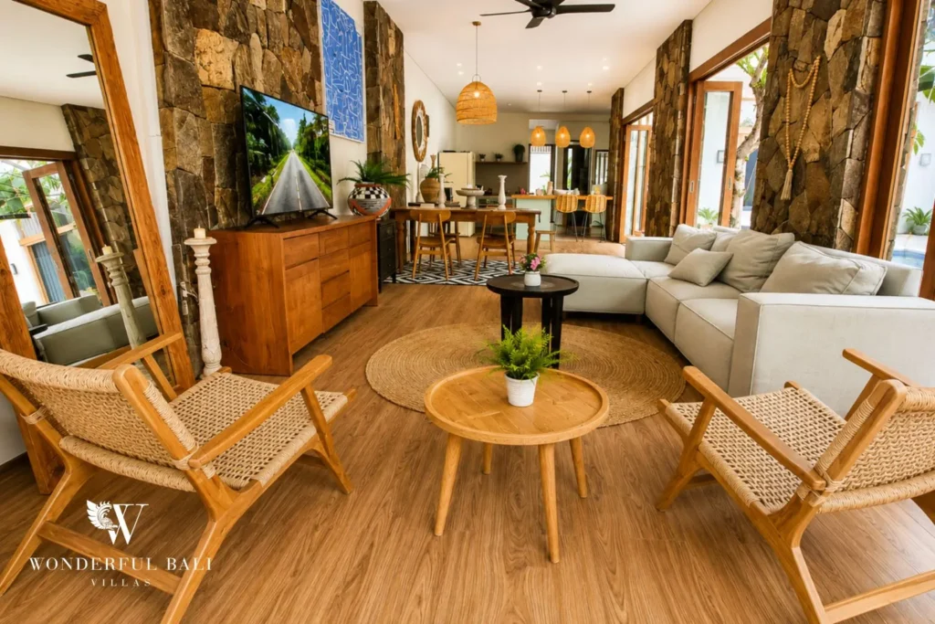 Living room with sofas, TV, timber chairs and stone feature wall at villa in Berawa, Bali