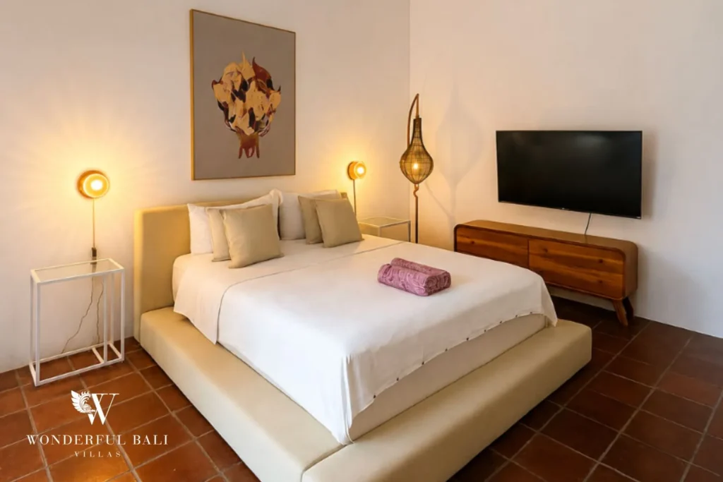 Bedroom with white bed, bedside lamp and TV in warm tones at villa in Canggu, Bali