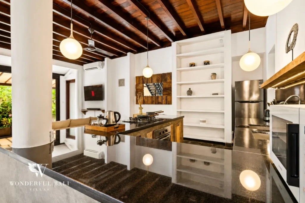 Kitchen with white cabinets, island and rattan pendants under timber ceiling at villa in Umalas, Bali