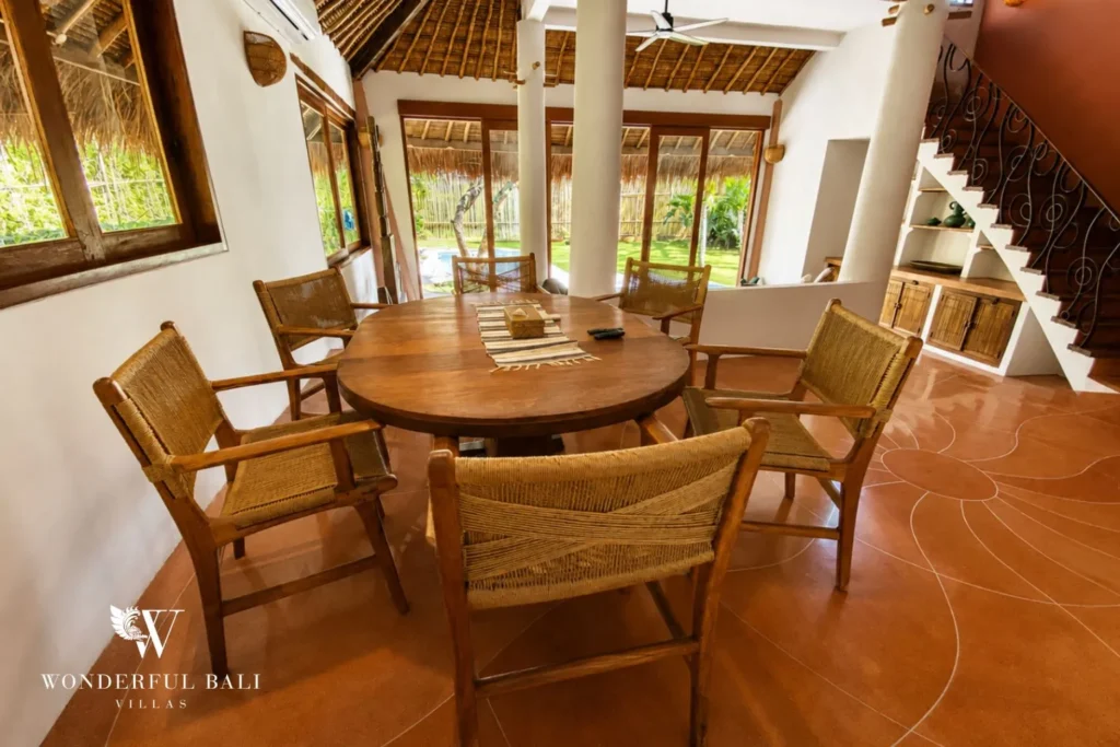 Dining with round timber table, rattan chairs and staircase at villa in Bumbak, Bali