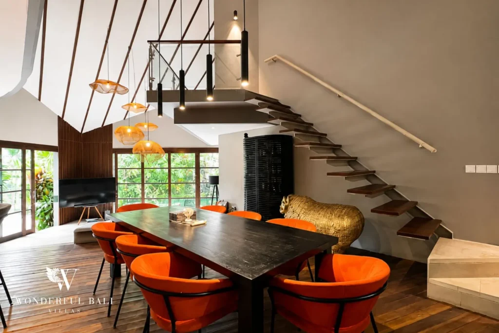 Dining table with orange chairs beside an open staircase at villa in Umalas, Bali