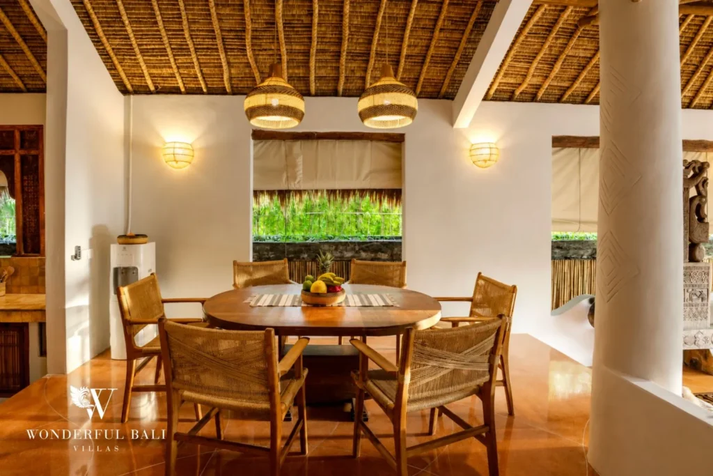 Round dining table with rattan chairs under a thatched roof at villa in Bumbak, Bali