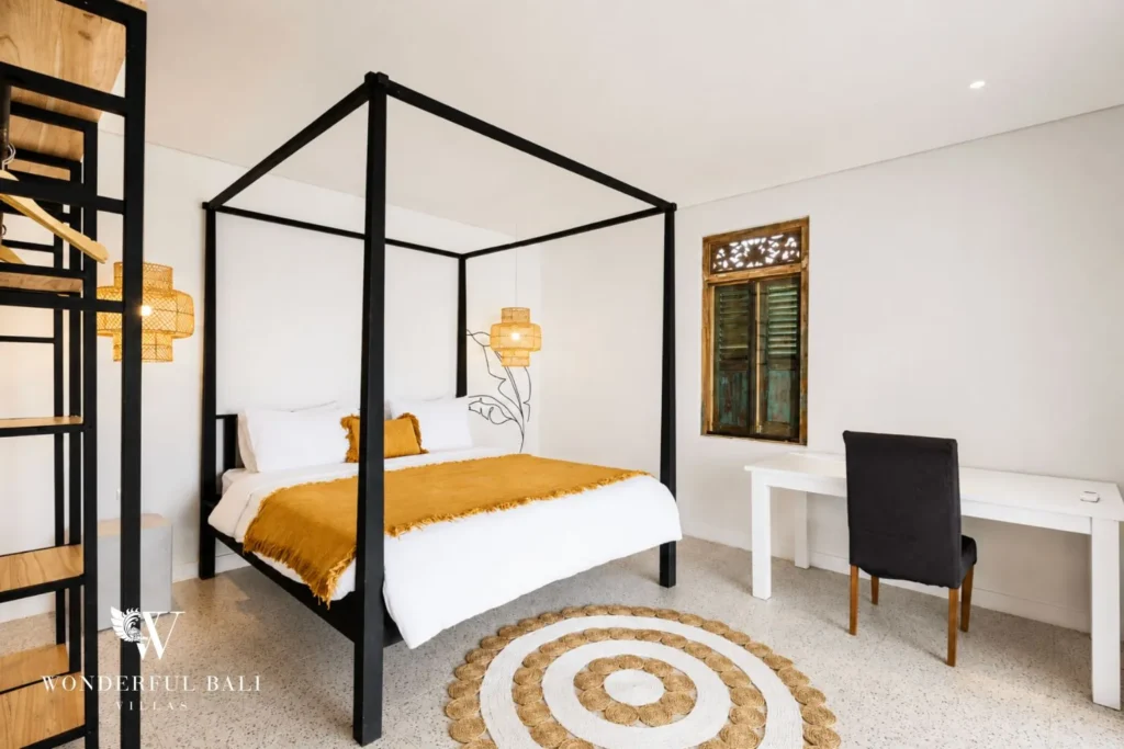Bedroom with black four-poster bed, mustard throw and desk at villa in Canggu, Bali