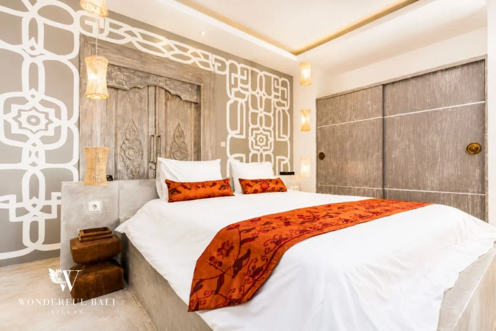 Bedroom with carved antique door headboard and orange batik accents at villa in Seminyak, Bali