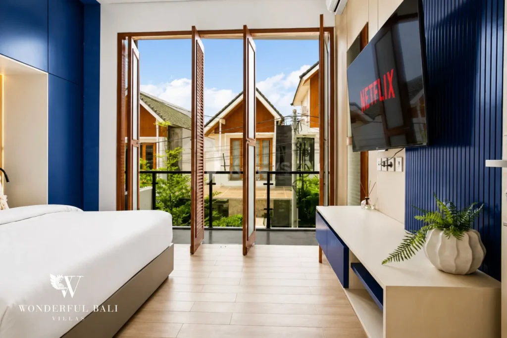 Bedroom with blue feature wall, white bed and wall TV at villa in Denpasar, Bali