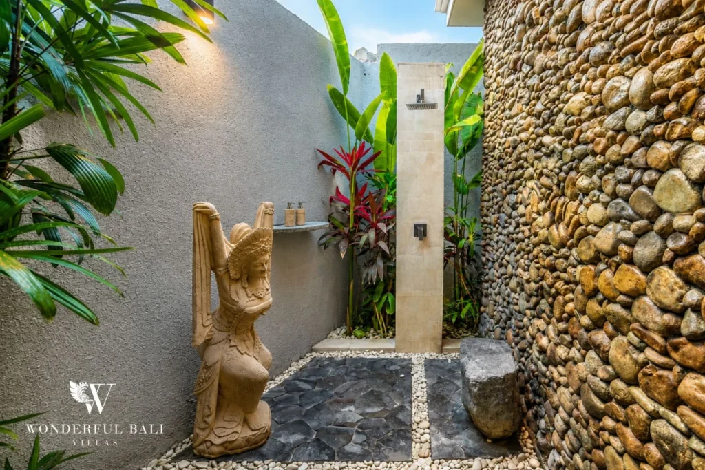 Outdoor shower with river stone wall and carved deity statue at villa in Seminyak, Bali