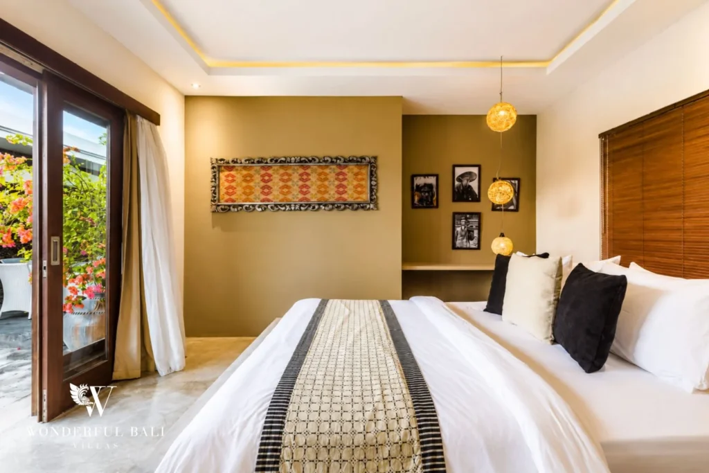 Bedroom with olive accent wall, Bali textile art and framed photographs at villa in Seminyak, Bali
