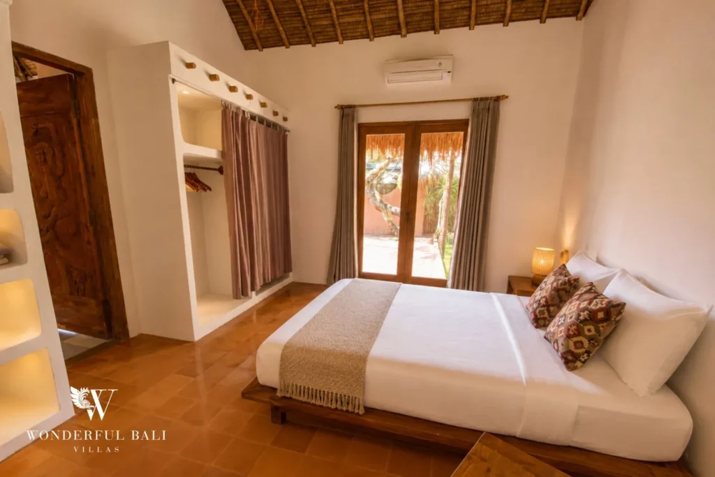 Bedroom with terracotta walls, white bed and timber window at villa in Bumbak, Bali