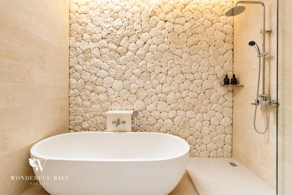 Bathroom with freestanding tub against a natural stone wall at villa in Canggu, Bali