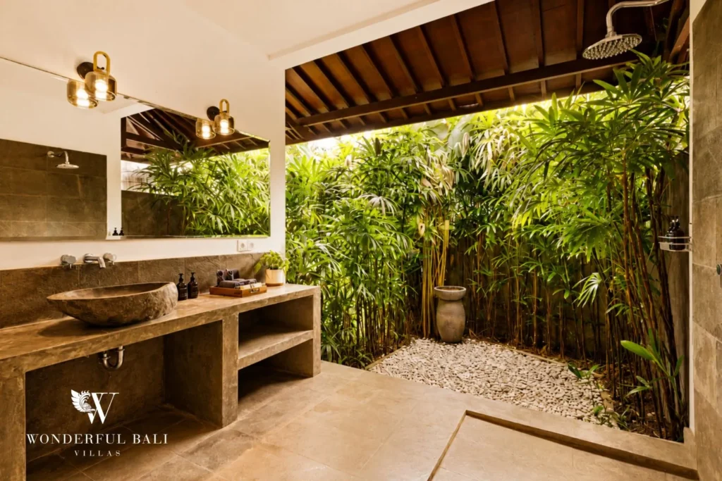 Open-air bathroom with timber vanity opening to a pebbled garden at villa in Umalas, Bali