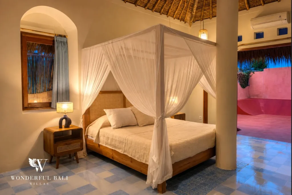 Bedroom with four-poster mosquito-net bed and accent seat at villa in Bumbak, Bali