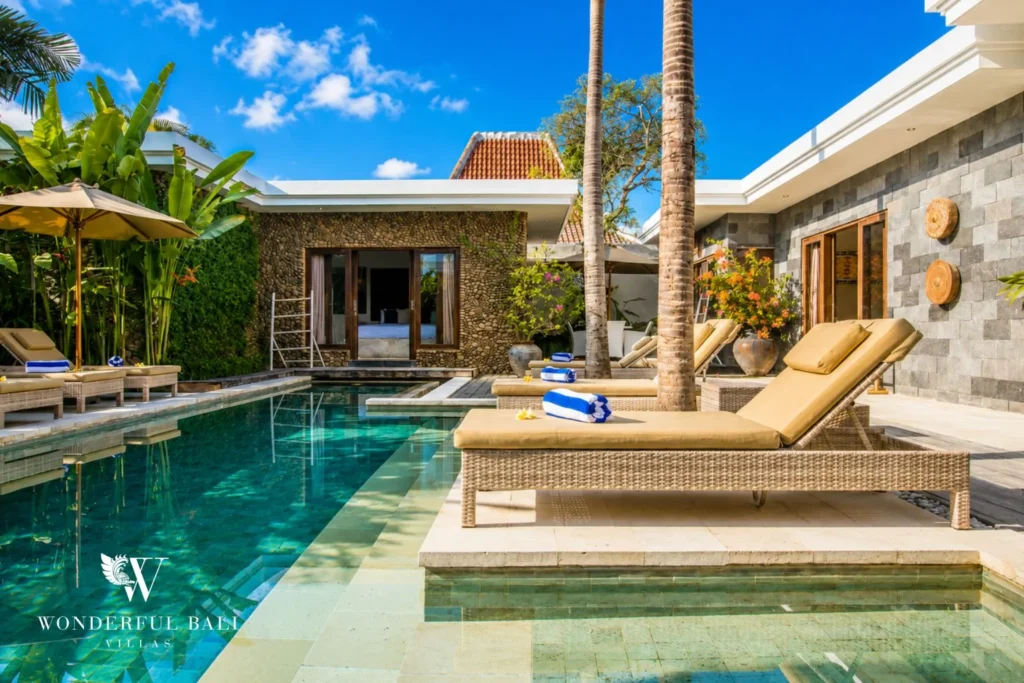 Lap pool with rattan loungers, frangipani trees and blue umbrella at villa in Seminyak, Bali