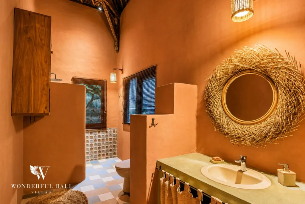 Terracotta bathroom with round woven mirror and vanity at villa in Bumbak, Bali