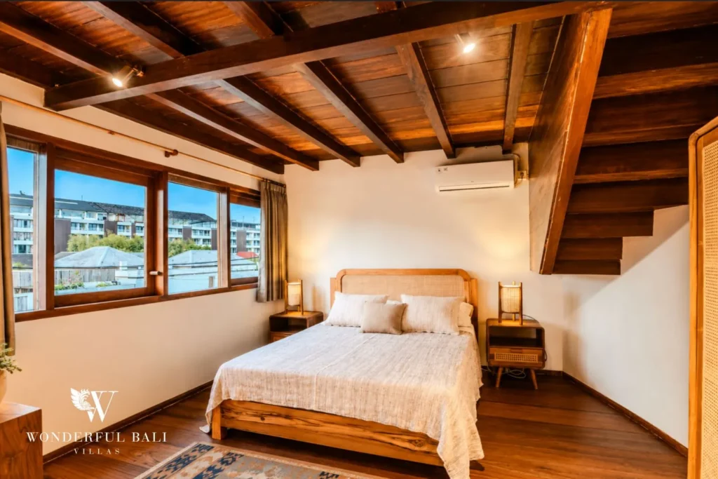 Bedroom with timber bed, thatched ceiling and window views at villa in Bumbak, Bali