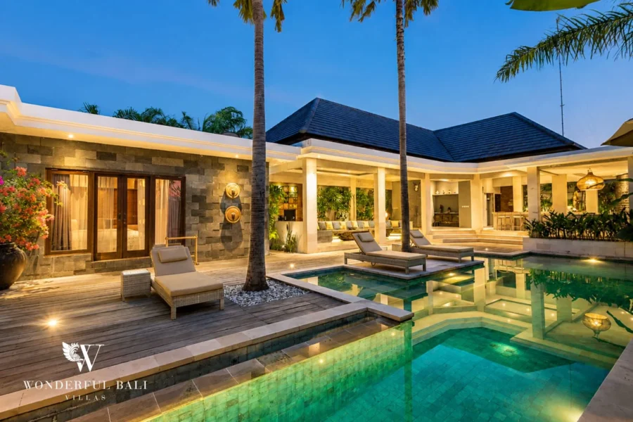 Pool at twilight with lit pavilions and central sun-deck at villa in Seminyak, Bali