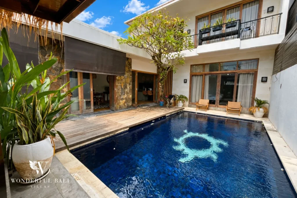 Pool with sun chairs and two-storey villa exterior in daylight at villa in Berawa, Bali