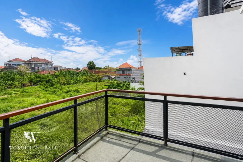 Balcony with railing overlooking open green fields at villa in Denpasar, Bali