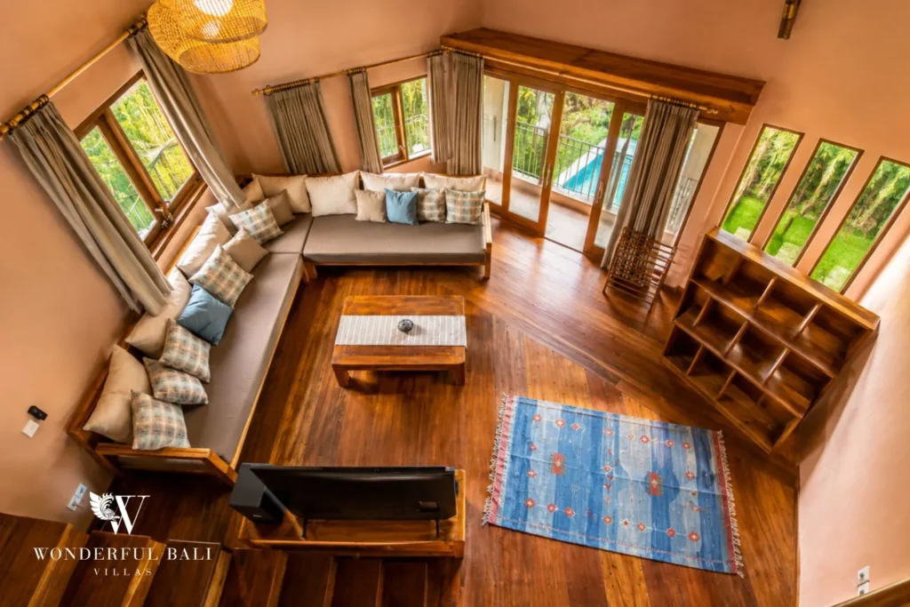 Loft lounge with sofa and timber floor under a thatched roof at villa in Bumbak, Bali
