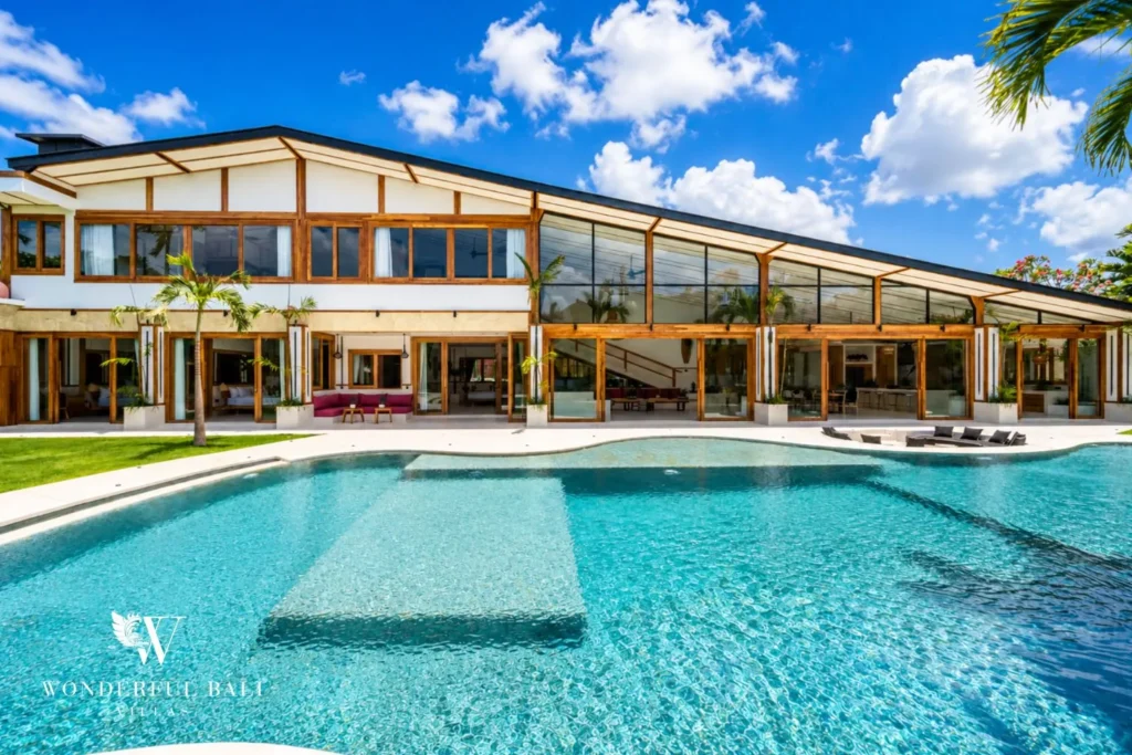 Pool and villa exterior with glass facade and sun loungers at family villa in Umalas, Bali