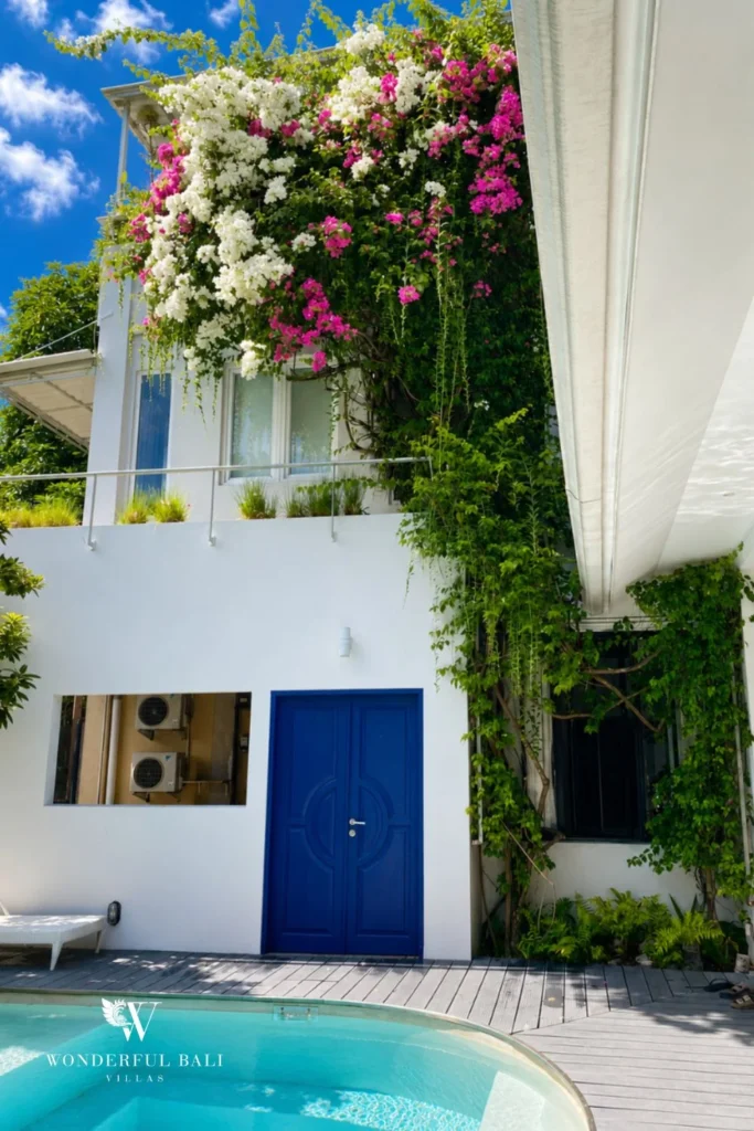 Bougainvillea-draped two-story facade with blue door at villa in Umalas, Bali
