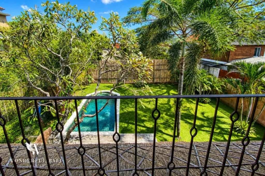 Pool and lush garden viewed through a railing at villa in Bumbak, Bali