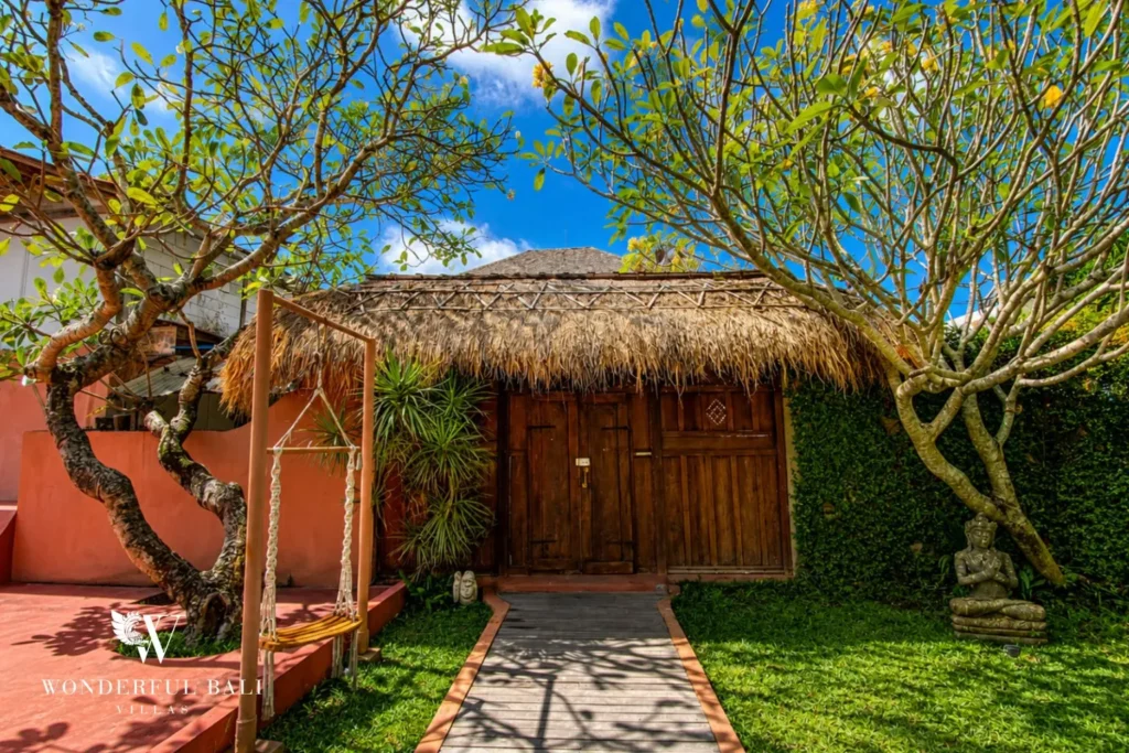 Garden with thatched bale, timber gate and lawn at villa in Bumbak, Bali