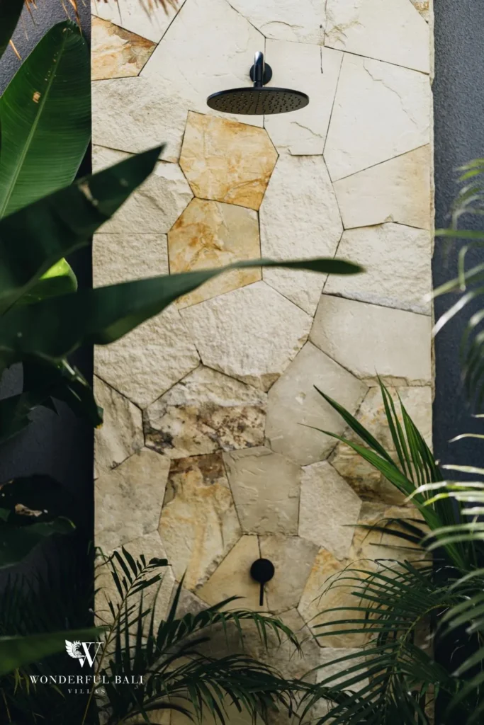 Outdoor shower against a natural stone wall with plants at villa in Seseh, Bali