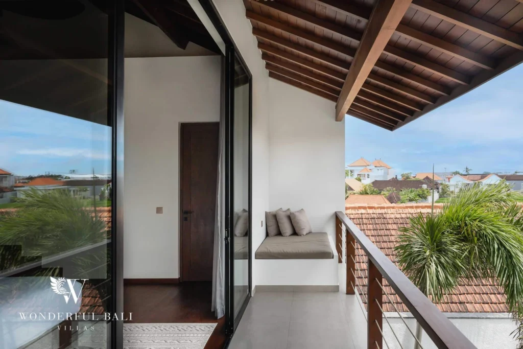 An upstairs balcony with a cushioned bench under a timber roof overlooking neighbouring rooftops and palms at a 2-bedroom villa in Canggu, Bali