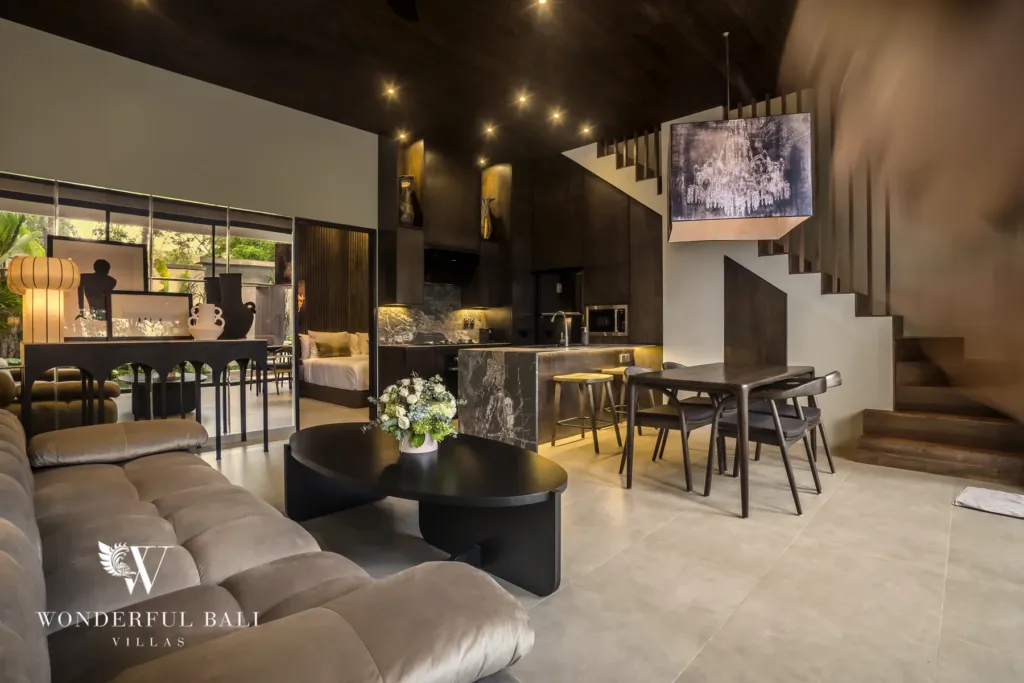 2BR villa for rent in Pererenan — living room, a double-height open-plan living space with a plush sofa, dining table, open kitchen and a staircase beneath lofty wood-panelled ceilings at a 2-bedroom villa