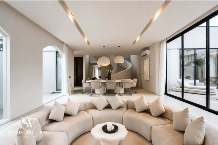Open-plan living and dining area of a modern 3-bedroom villa in Umalas, Bali, with a curved sunken lounge, stone dining table and spiral staircase