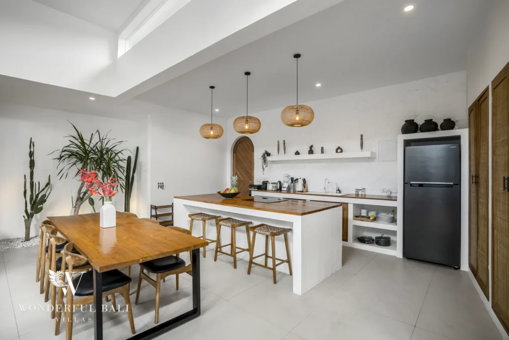 An open-plan kitchen with a white island, wooden countertop, rattan pendant lights and a dining table with woven chairs at a 3-bedroom villa in Bingin, Uluwatu, Bali