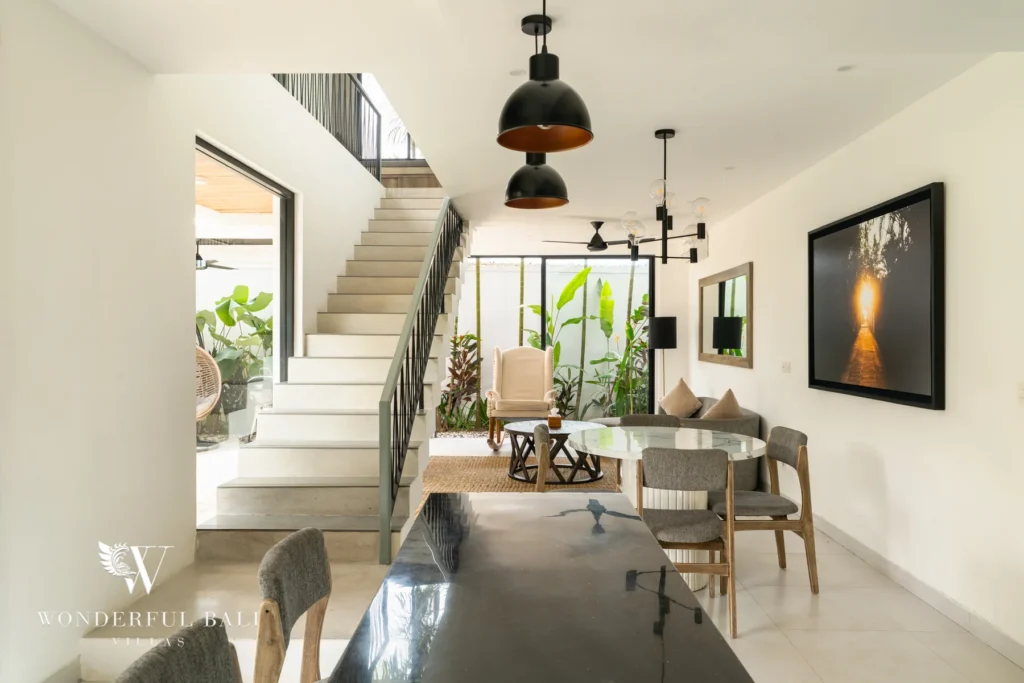 An open-plan interior with a staircase, glass-topped dining table, black pendant lights and a marble bar counter opening to a planted courtyard at a 3-bedroom villa in Berawa, Bali