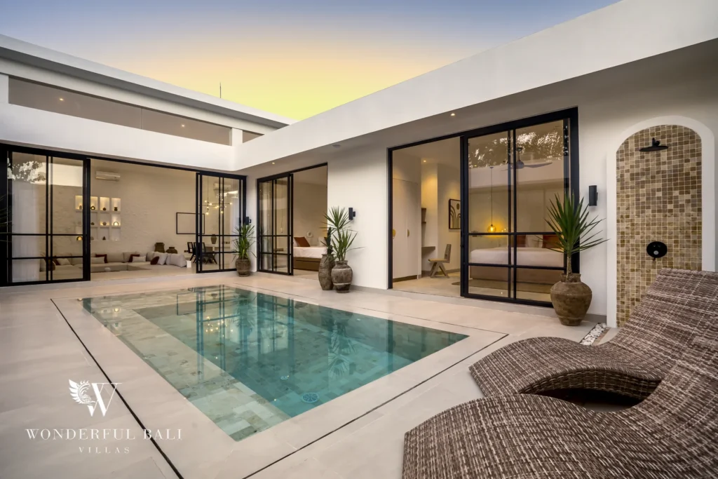 A private pool set in an open-air courtyard at dusk surrounded by glass-walled rooms and a woven lounge chair at a 3-bedroom villa in Bingin, Uluwatu, Bali