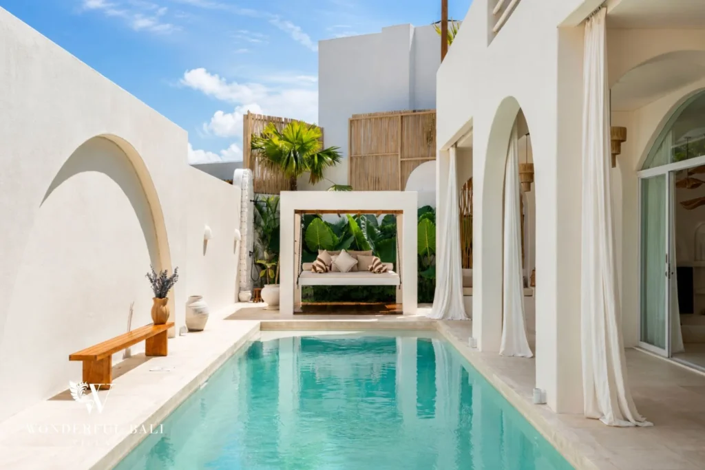 A private turquoise pool bordered by white arched walls, a cushioned hanging daybed and a wooden bench, at a 2-bedroom villa in Bingin, Uluwatu, Bali