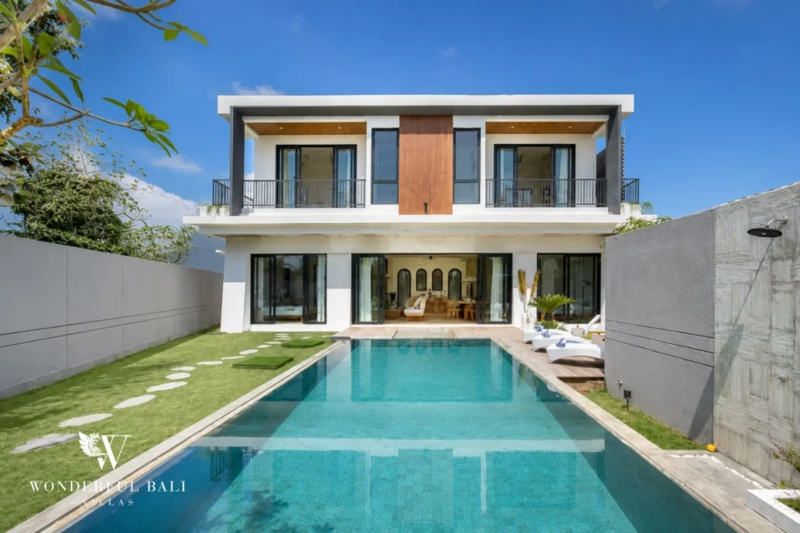 A modern two-storey villa facade with a long private pool, stepping-stone lawn and double-height glass living area at a 4-bedroom villa in Pererenan, Bali