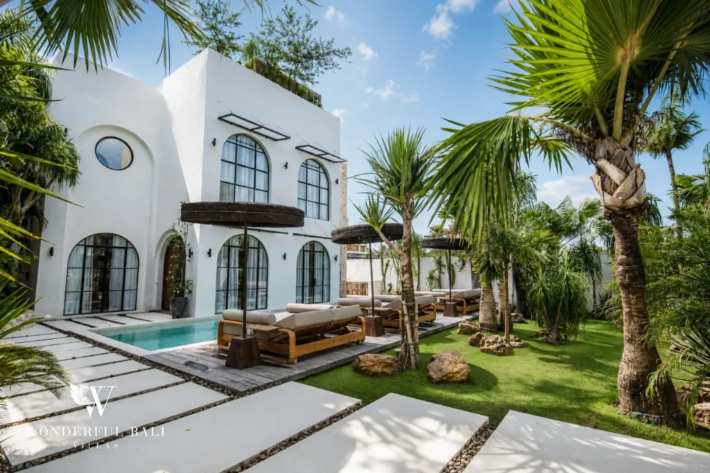 White Mediterranean villa with arched windows beside a pool and palm garden in Canggu Bali