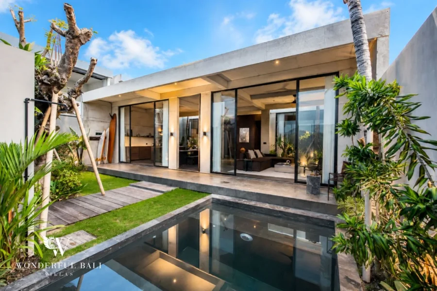 Modern industrial villa with a private pool, timber deck and open-plan living area behind black steel-framed glass doors under a blue sky at a 2-bedroom villa in Seseh, Bali