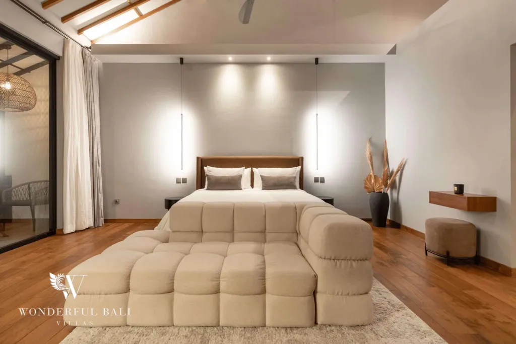 2BR villa for rent in Pererenan — bedroom, a spacious bedroom with a wood-framed bed, a cream tufted daybed at its foot and a lofty battened ceiling above warm timber floors at a 2-bedroom villa