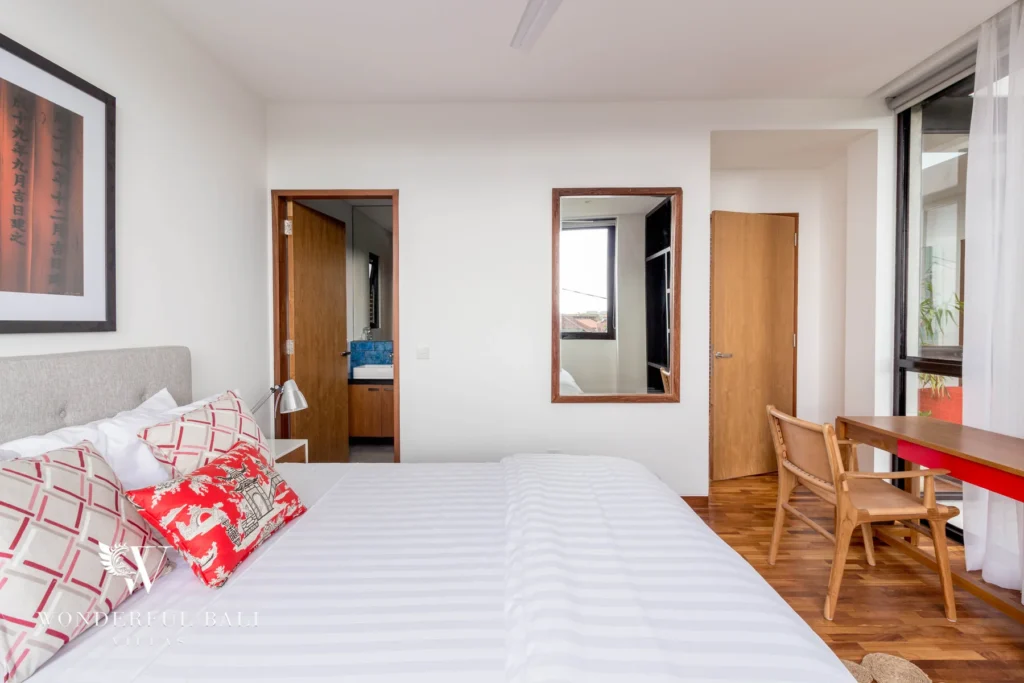 A bedroom showing a timber desk, wall mirror and an open door leading through to an en-suite bathroom at a 4-bedroom villa in Batu Bolong, Canggu, Bali